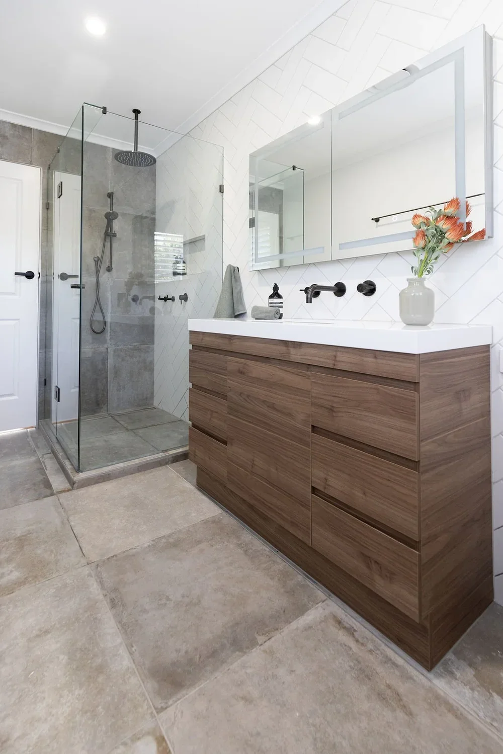 Full bathroom view with walnut floating vanity, herringbone tile, frameless glass shower, and gray stone floor — Issaquah WA bathroom remodel