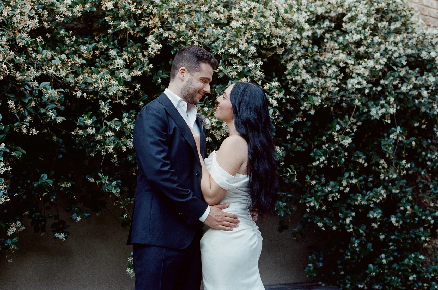 Couple facing each other in front of a wall of white jasmine