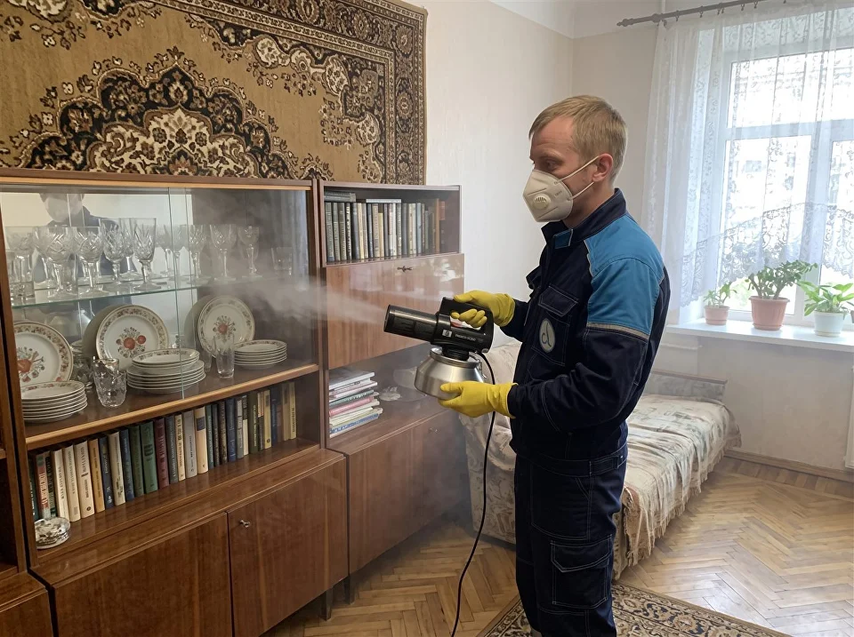 Мастер обрабатывает сухим туманом комнату со старой мебелью и коврами