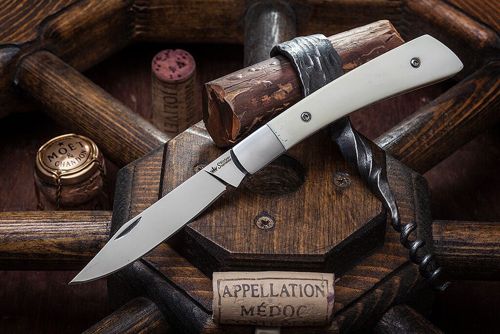 White-handled Kizlyar Supreme folding knife displayed on a wooden table