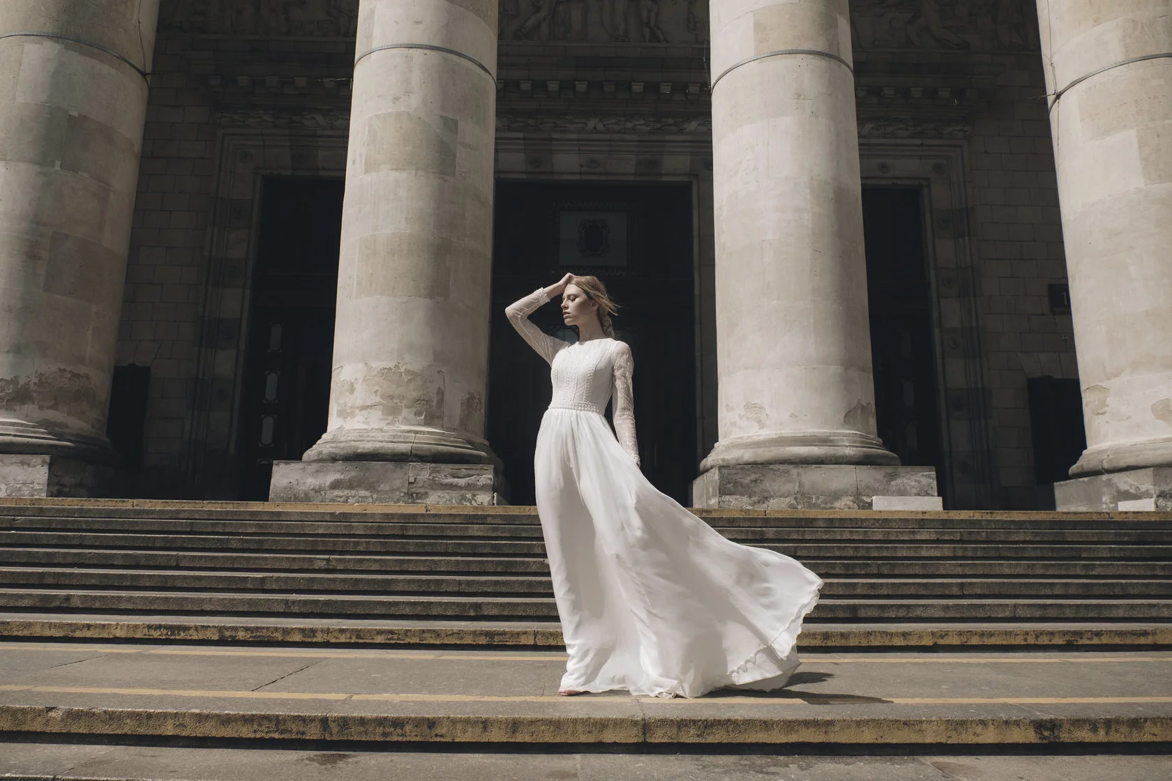 Bride in a long-sleeved wedding dress on the steps of a columned building