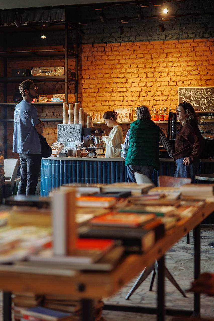 Гости клуба у барной стойки, на переднем плане стол с книгами