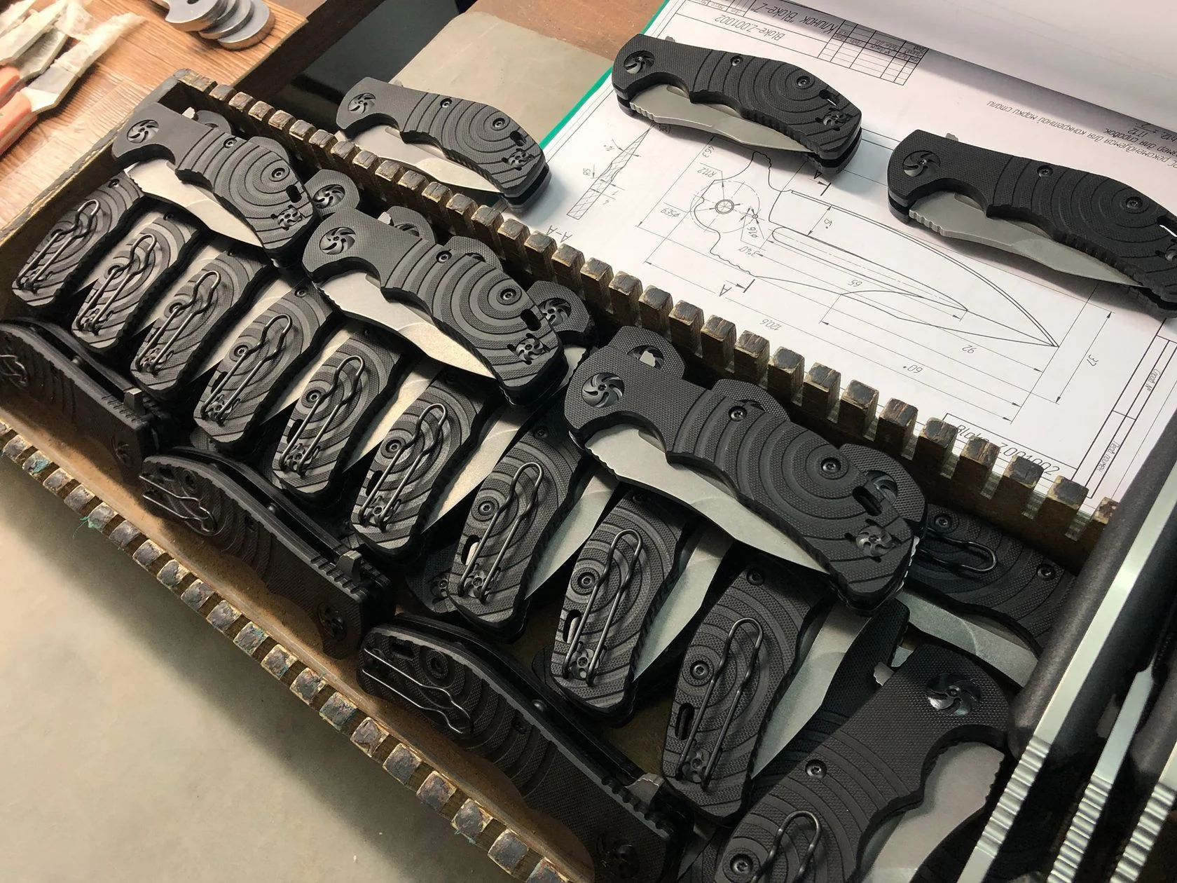 Kizlyar Supreme folding knives beside technical drawings during production