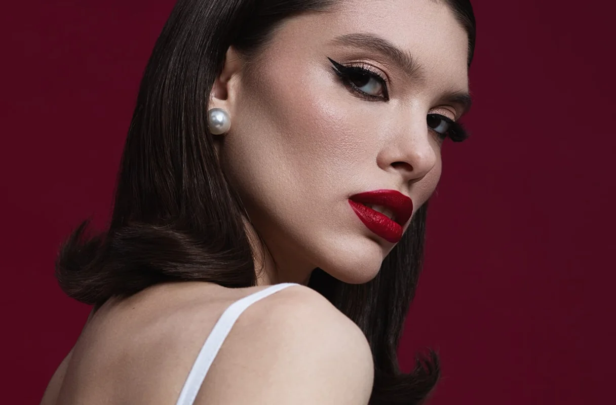 Beauty close-up with sculpted dark hair, winged eye makeup, red lipstick and a pearl earring