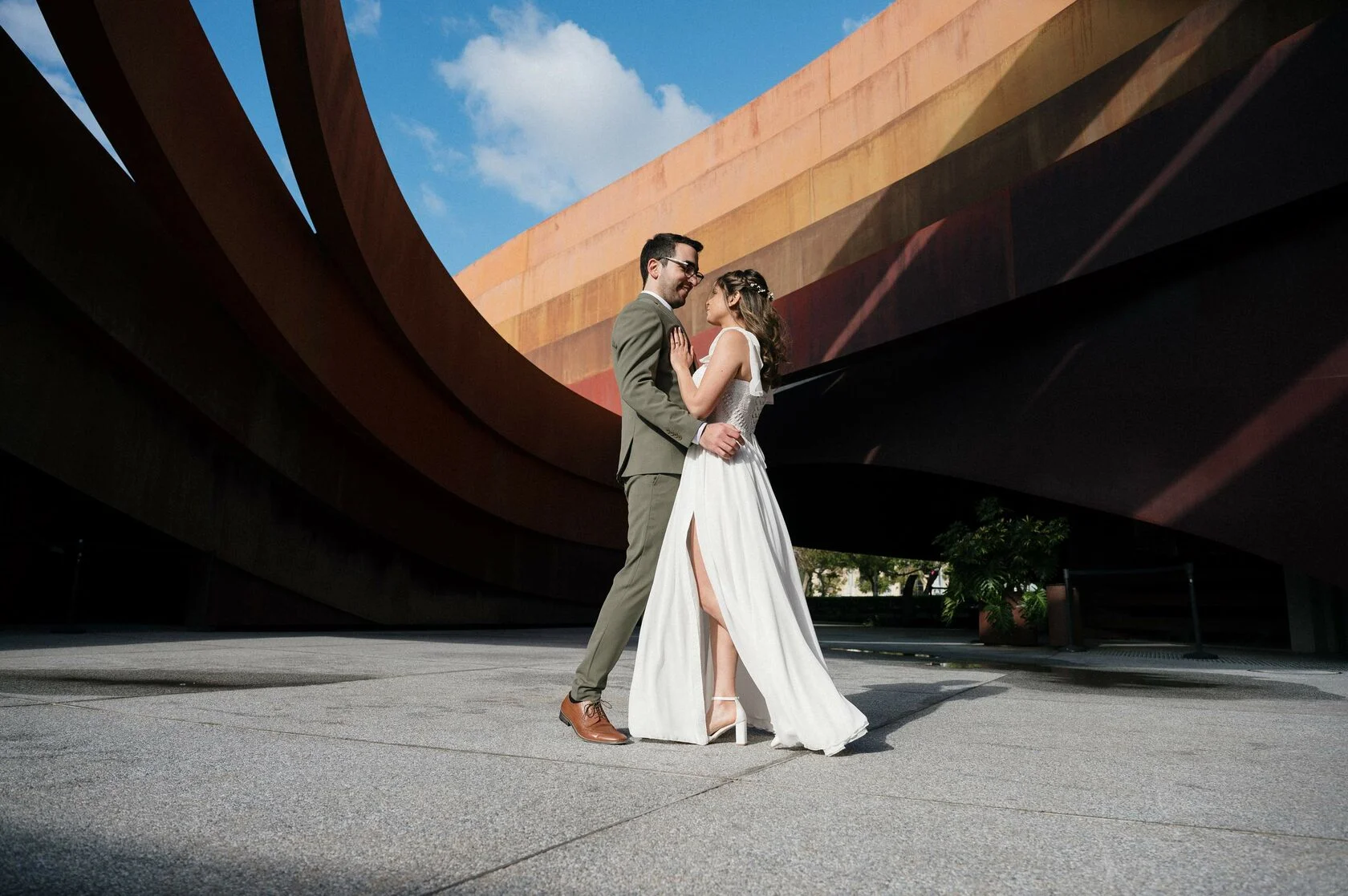 Bride and groom embrace under the rust-red curves of the Design Museum Holon