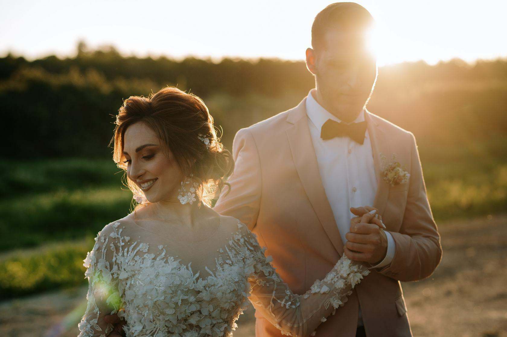 Bride and groom in a pink suit walk hand in hand in the golden sunlight