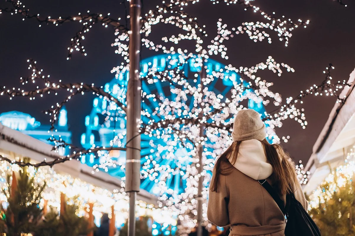 A visitor under strings of Christmas lights at night