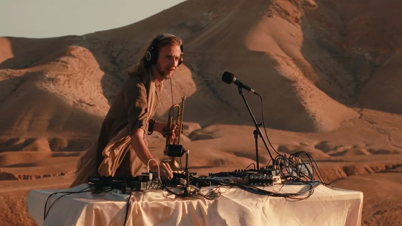 Omasoul with headphones and a trumpet at a mixing desk in the Judean Desert at sunset