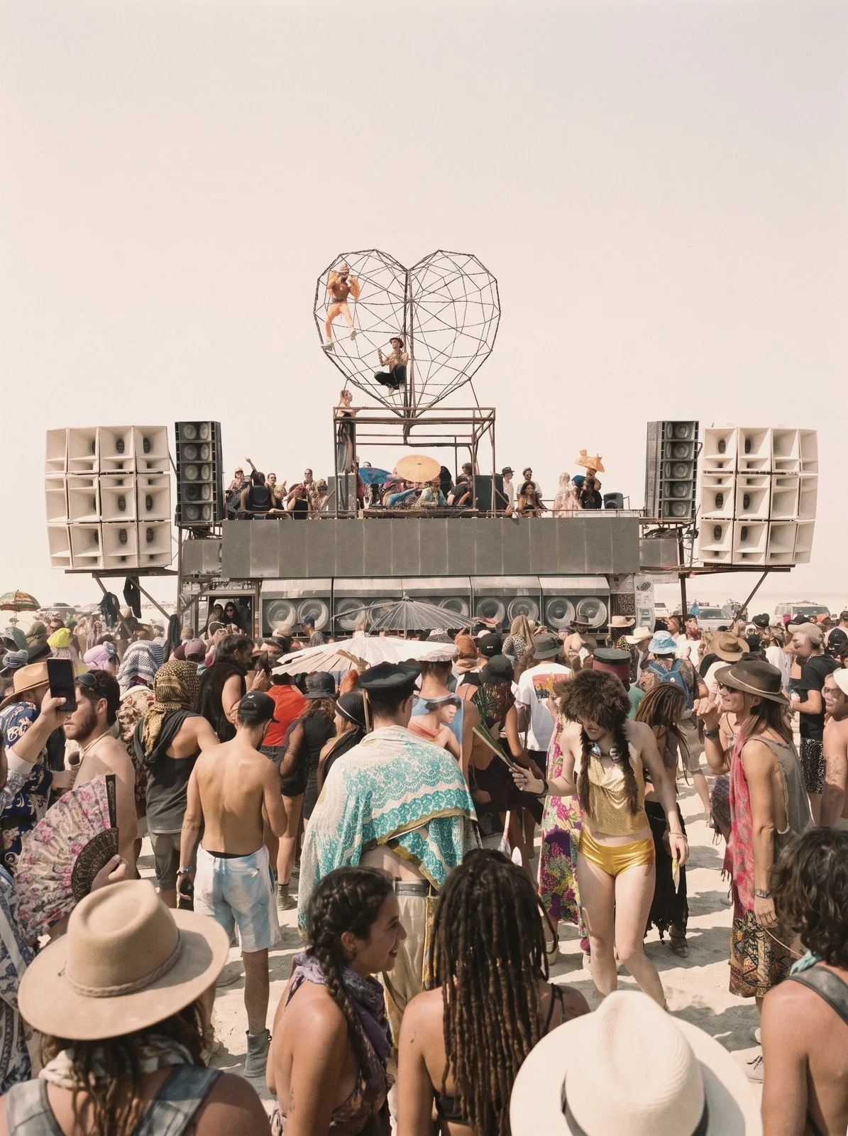 Crowd dancing in front of a desert art car stage with speaker walls and a steel heart sculpture