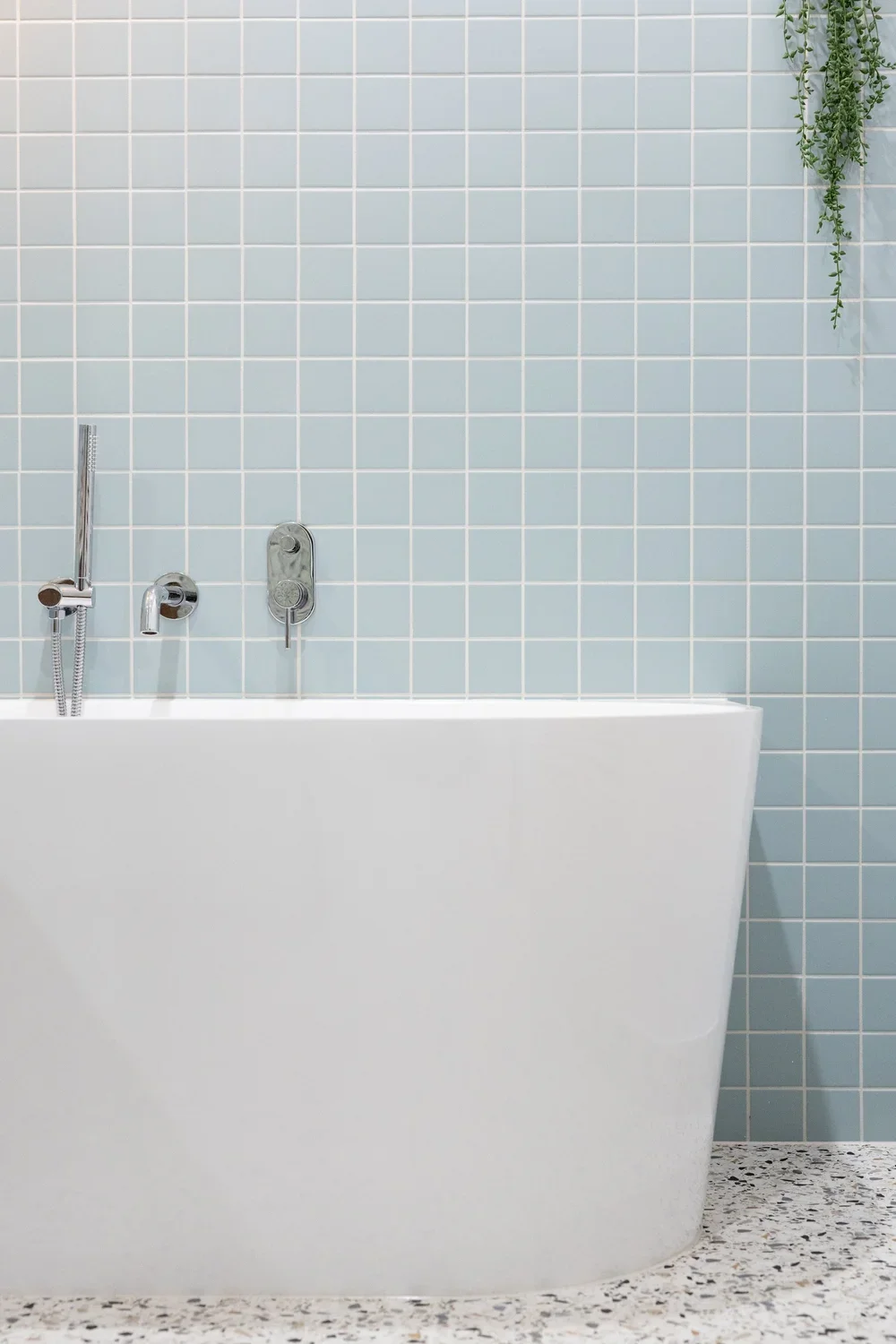 Freestanding white tub with chrome fixtures on blue subway tile wall and terrazzo floor — bathroom remodeling Redmond WA